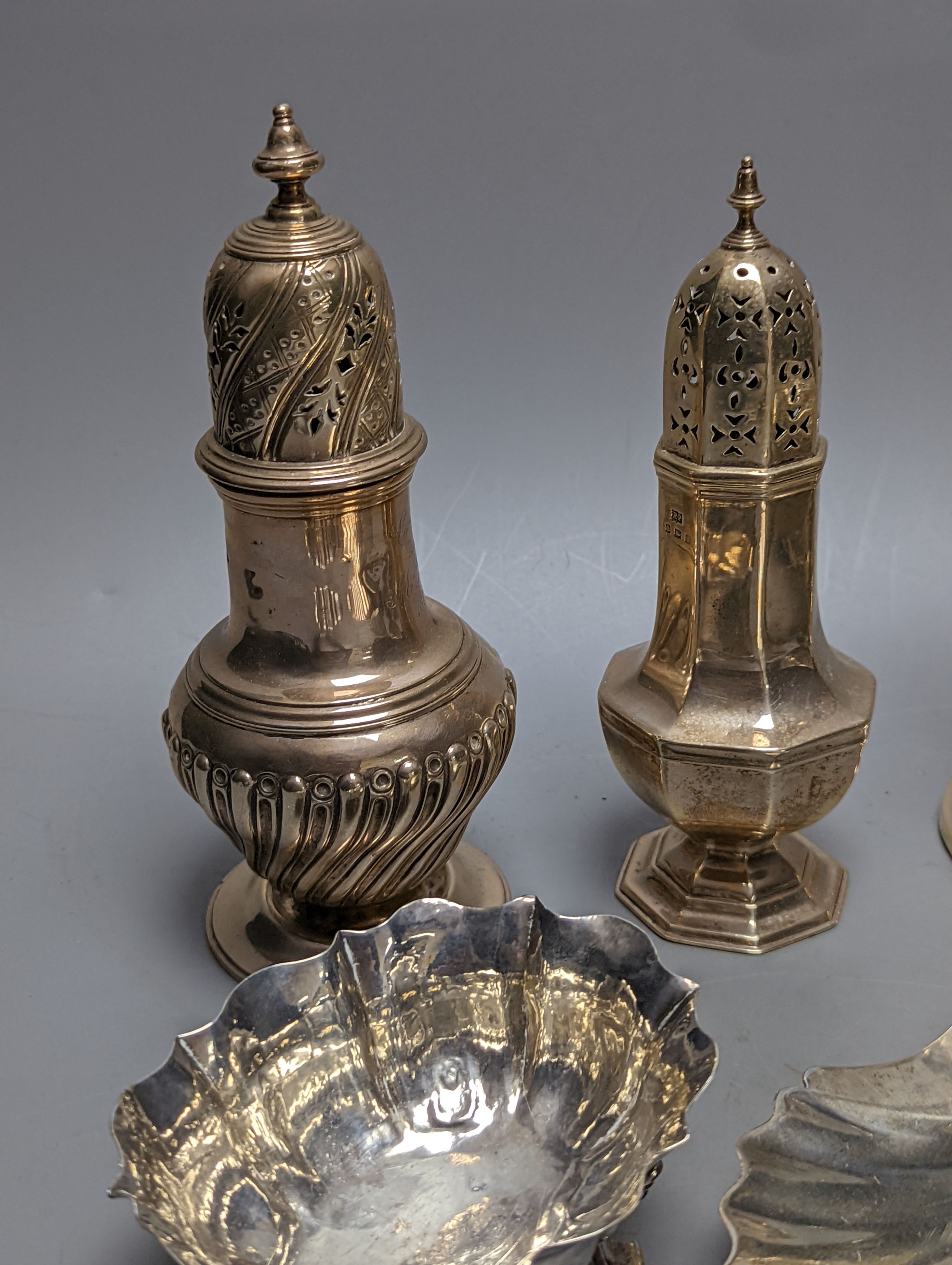 A mixed collection of silver to include a George III silver butter shell, London, 1799, a small cigarette box, two casters, a pair of slender candlesticks (loaded) and two small bowls including white metal